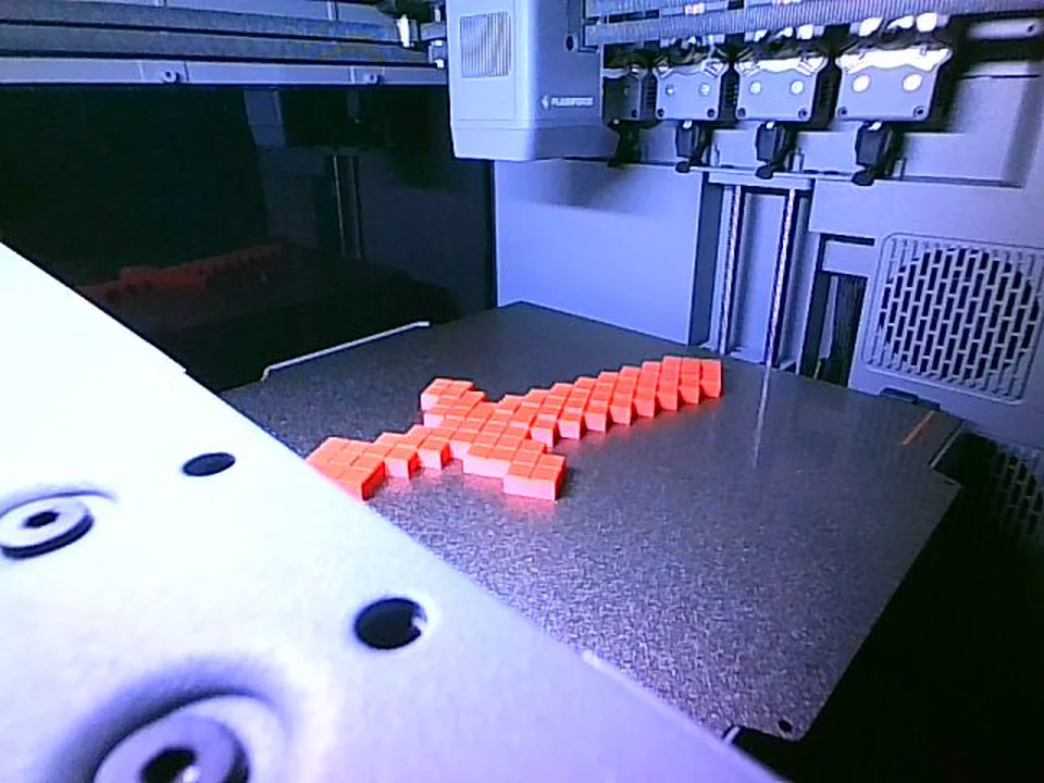 Das fertige rote Pixelschwert liegt auf der Druckplatte, darüber die vier Druckköpfe.