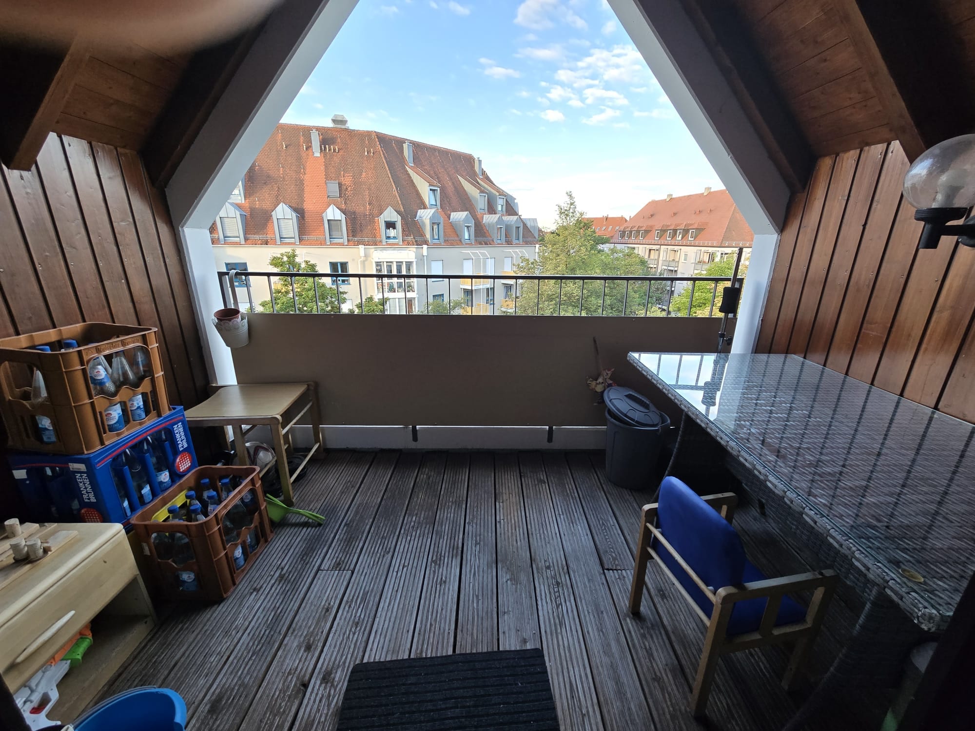 Derselbe Balkon nach dem Aufräumen: freie Holzdielen, rechts der Gartentisch mit Glasplatte, dahinter der Blick über die Nachbardächer