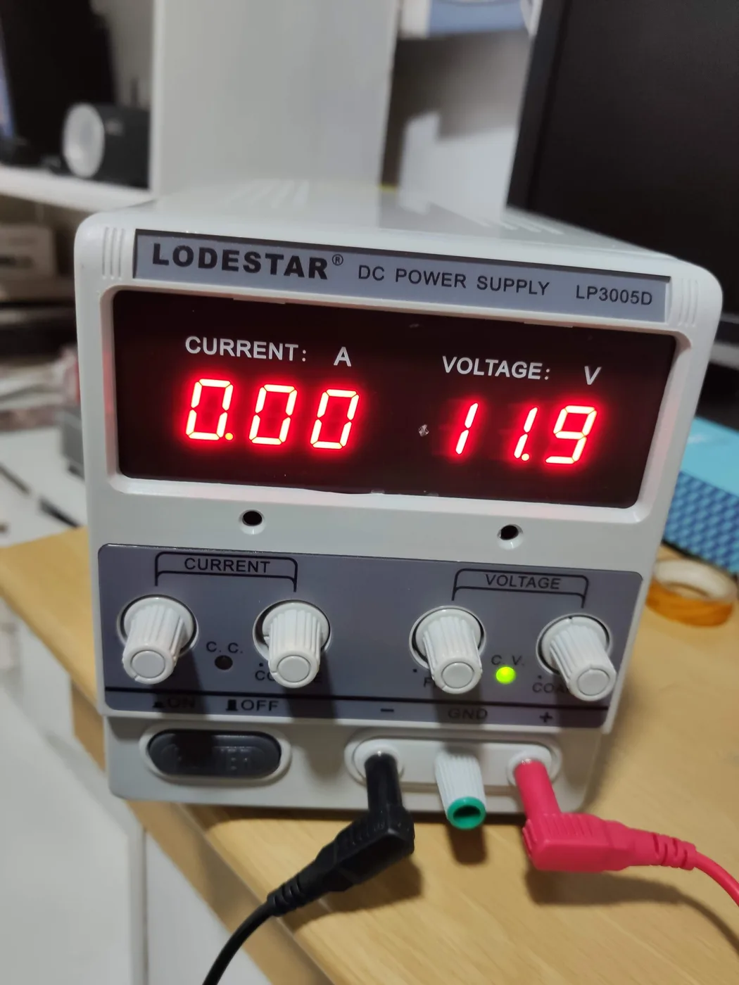 Labornetzteil mit roter Siebensegment-Anzeige für Strom und Spannung, vier Drehknöpfen und angesteckten Messleitungen auf einem Schreibtisch