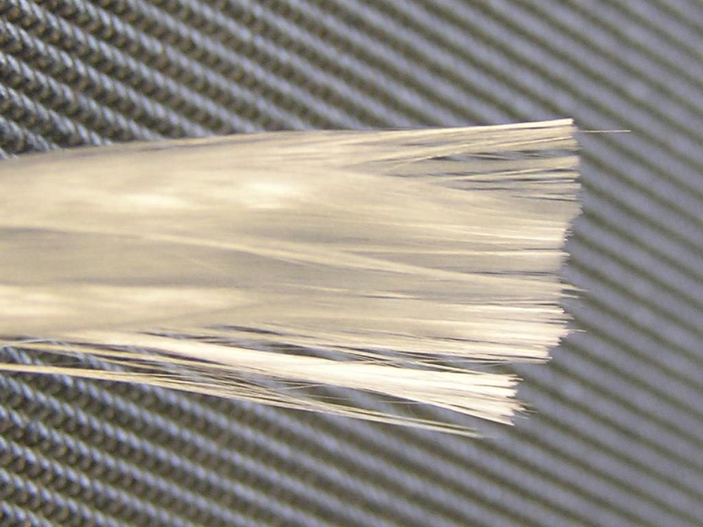 B&uuml;ndel heller Glasfaser-Roving-Str&auml;nge auf einem dunklen Gewebe