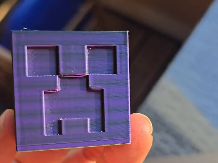 Eine Hand hält eine kleine lila Box mit vertieftem Creeper-Gesicht, die Druckschichten sind als feine Linien zu sehen